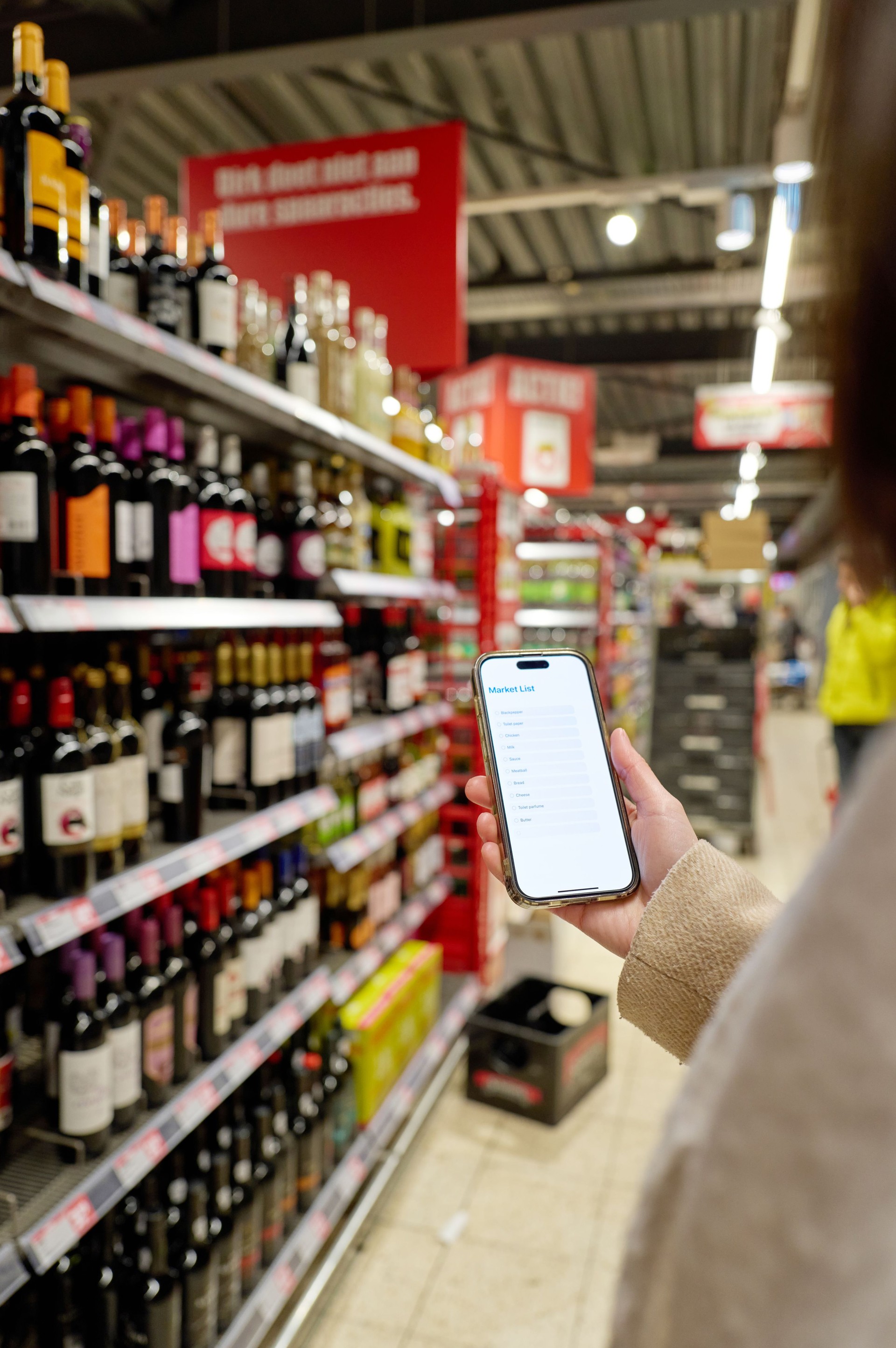 Woman using smartphone and shopping list app in supermarket alcohol section